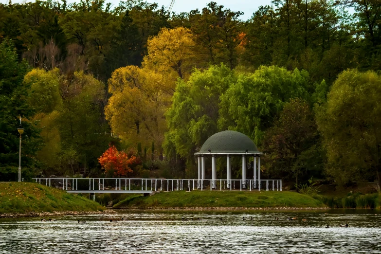 the gazebo is at the edge of the lake surrounded by trees