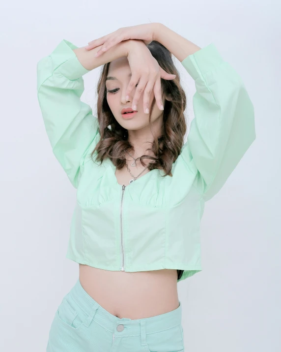 young woman in a light green cropped jacket, with her hands on the head