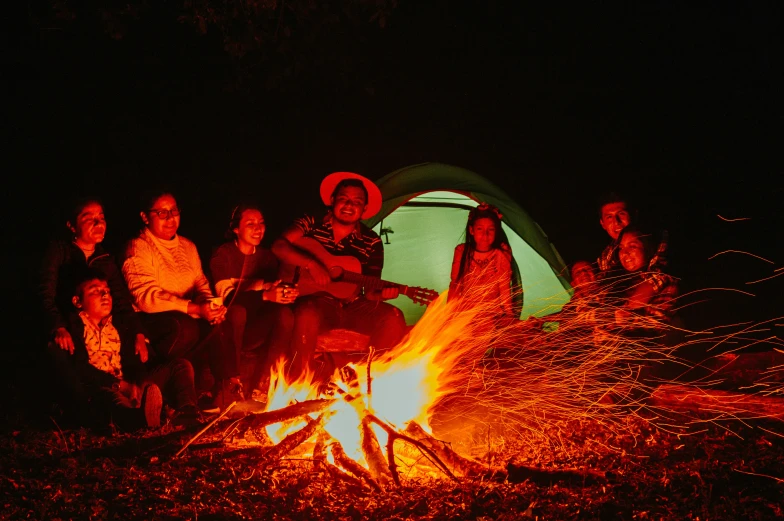 a family sits in front of a tent near a fire while the family is camping