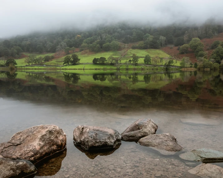 rock strewn in the foreground on top of a mountain overlooking a lake with green hills and fog