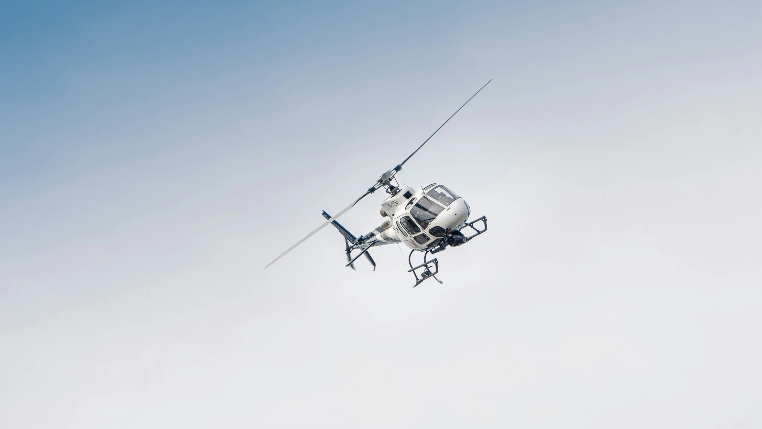 a helicopter flying in a blue sky holding onto a cable