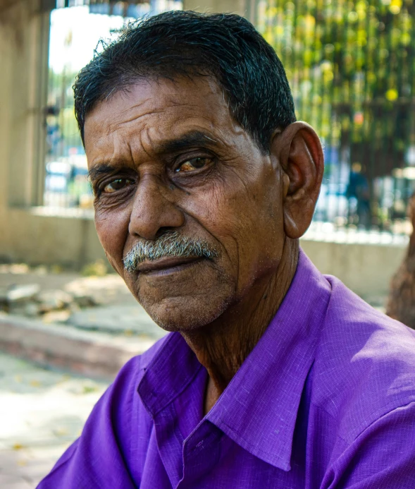 an old man in a purple shirt is sitting down