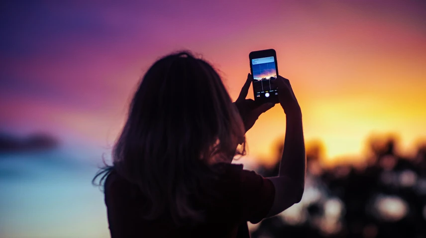 woman using her cell phone at sunset to take pos