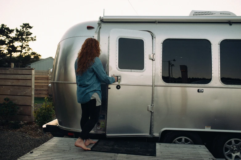 woman leaning against the front door of a silver airstream