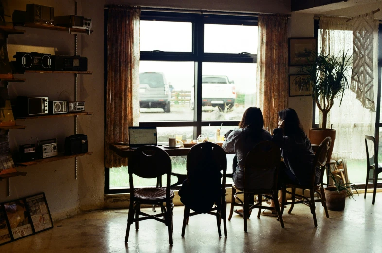 two women are seated at a table and looking outside the window