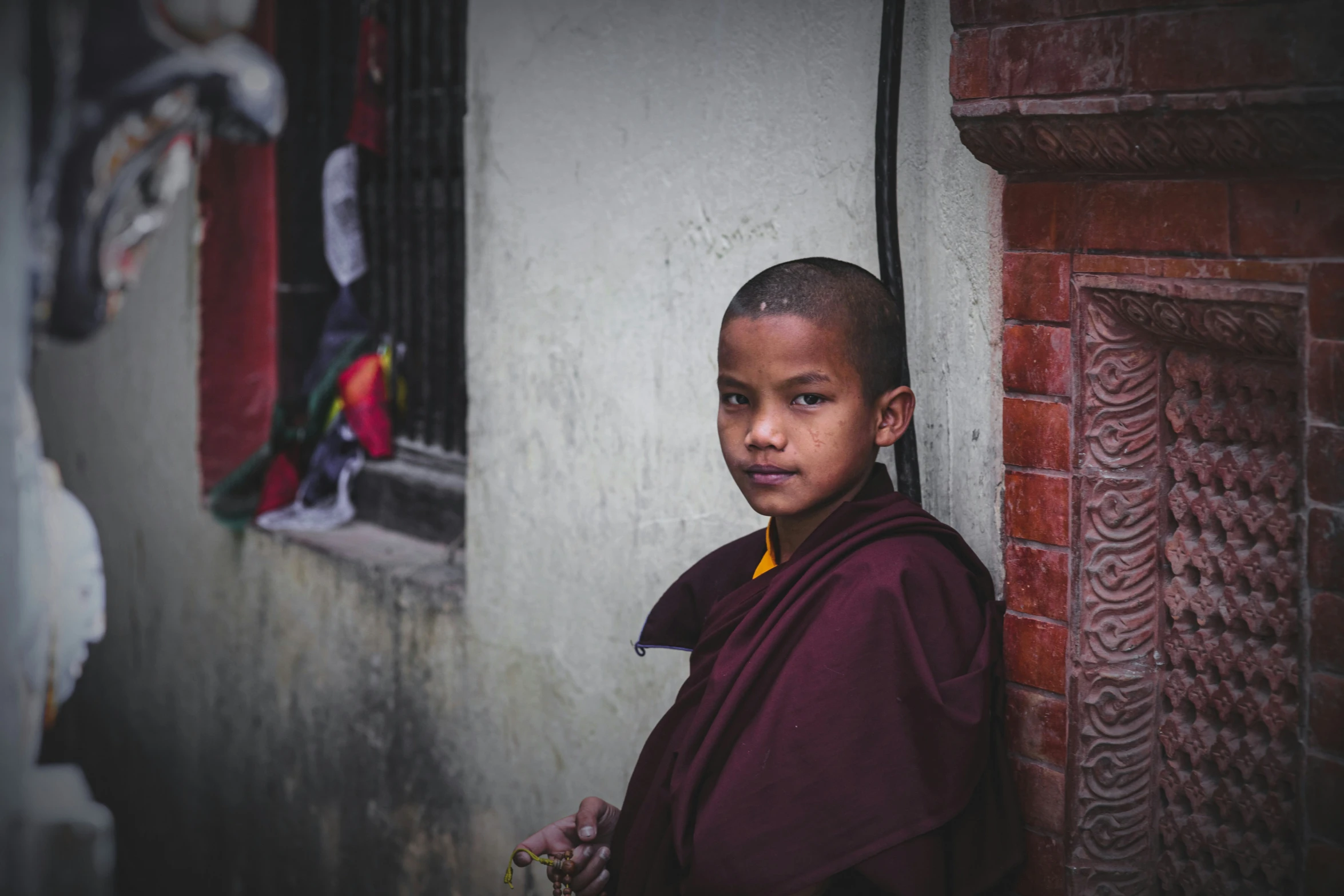 a boy in a monk robe standing next to a brick building