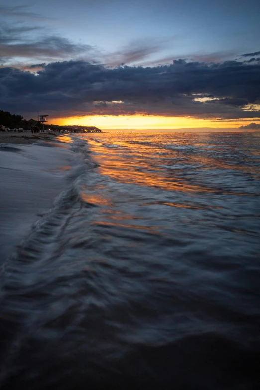 the sun setting on a beach with waves crashing