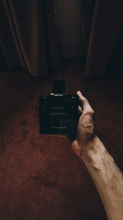 a man is holding up his own black cologne bottle