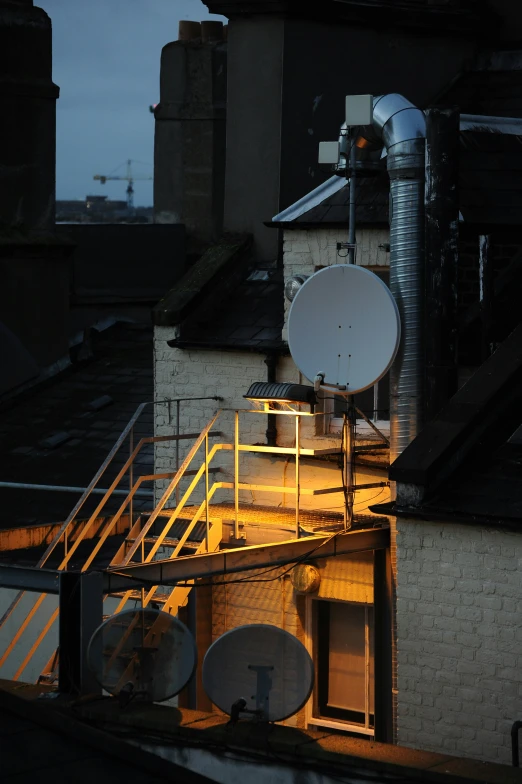 satellite dish outside at dusk on rooftop with buildings and chimneys