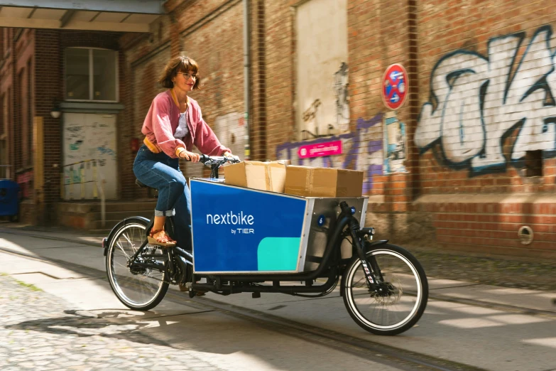 woman riding a bicycle with the front basket attached to a cargo cart on an alley way