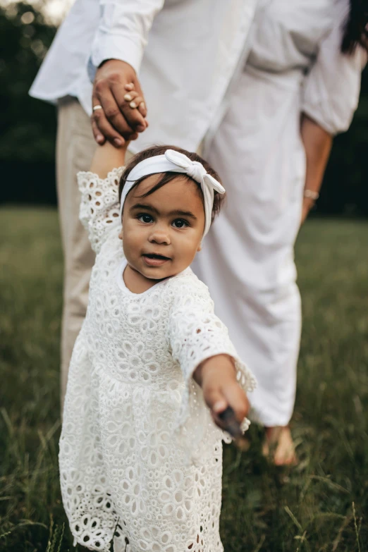 a little girl in white holding her fathers hands