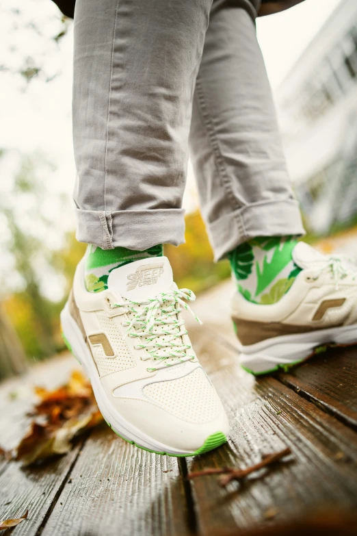 person in grey pants standing on wooden deck with green and white shoes