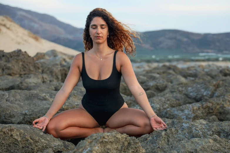 a woman wearing a swimsuit is meditating on some rocks