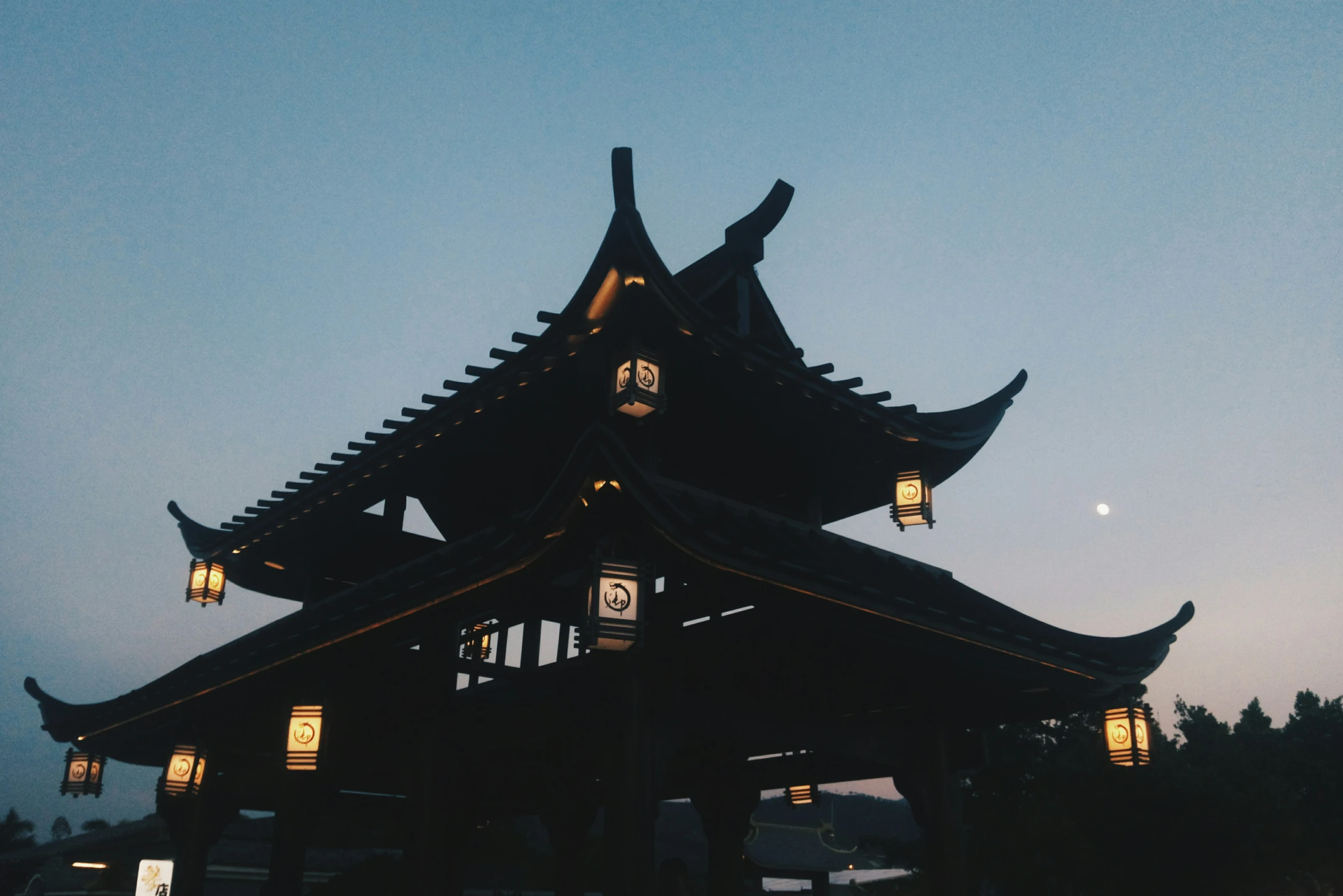 an oriental building lit up at night with a full moon in the sky