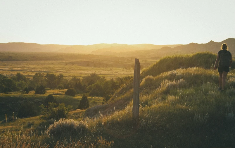 a lone woman standing on top of a hillside next to a fence