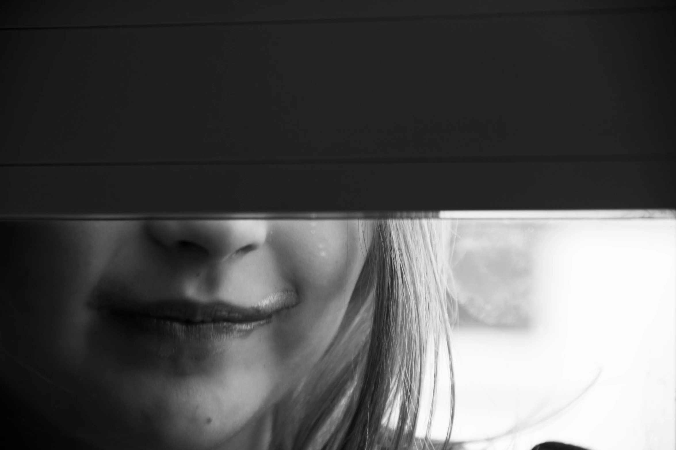 a girl has long dark hair and she is looking at the camera through a blind