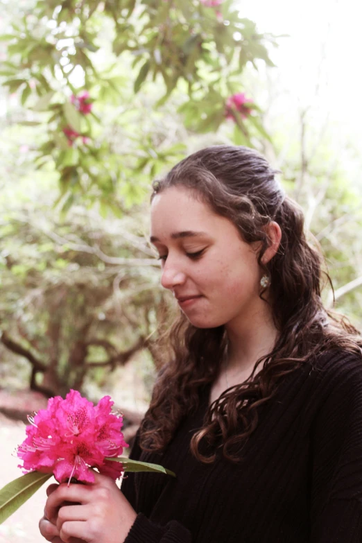 a woman is holding a pink flower and looking at it