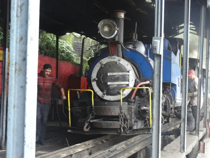 a steam train parked under a bridge with people looking at it