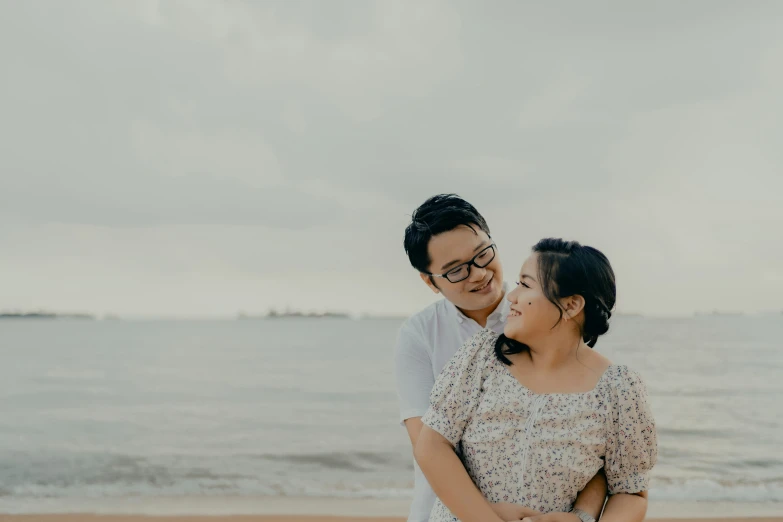 two people standing on a beach with the ocean in the background