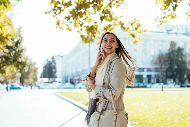 a smiling girl talking on a phone next to a park