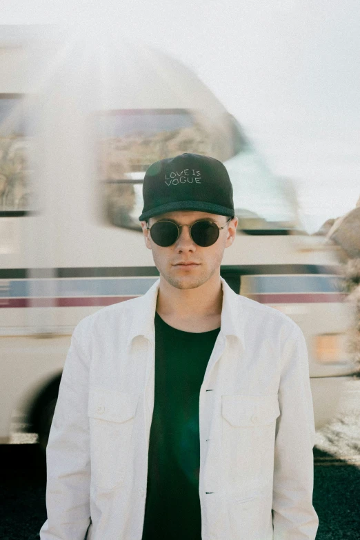 a man wearing sunglasses and a hat standing by a bus