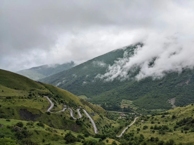 mountains are covered in cloud and hills with green grass