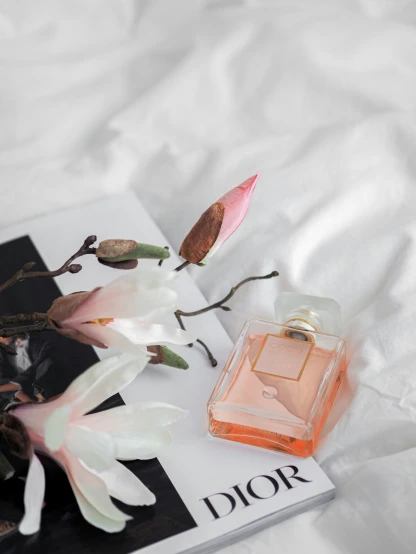 a bottle of perfume and a flower sitting on top of a book