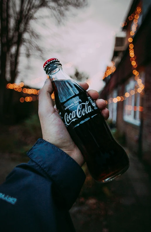 a person's hand holding a bottle with a lighted facade in the background