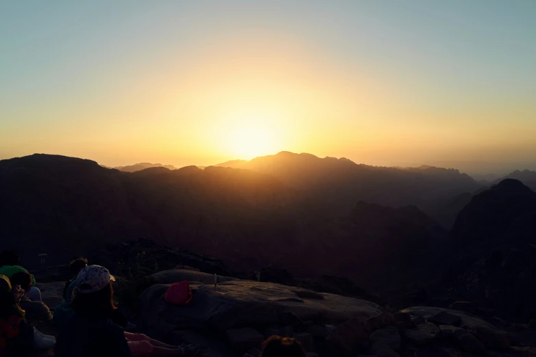 sunset in the mountains with many people sitting at the edge