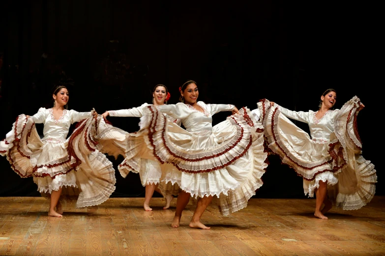 five women in long white dress are dancing on a stage