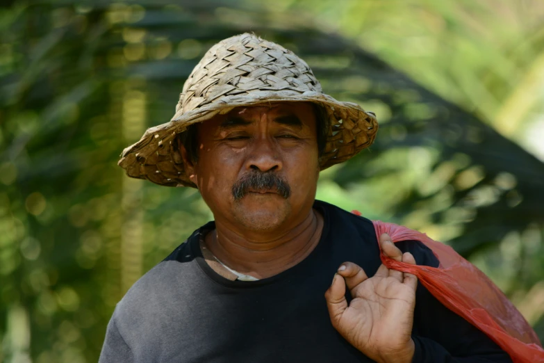 an asian man with a straw hat on holding a bag