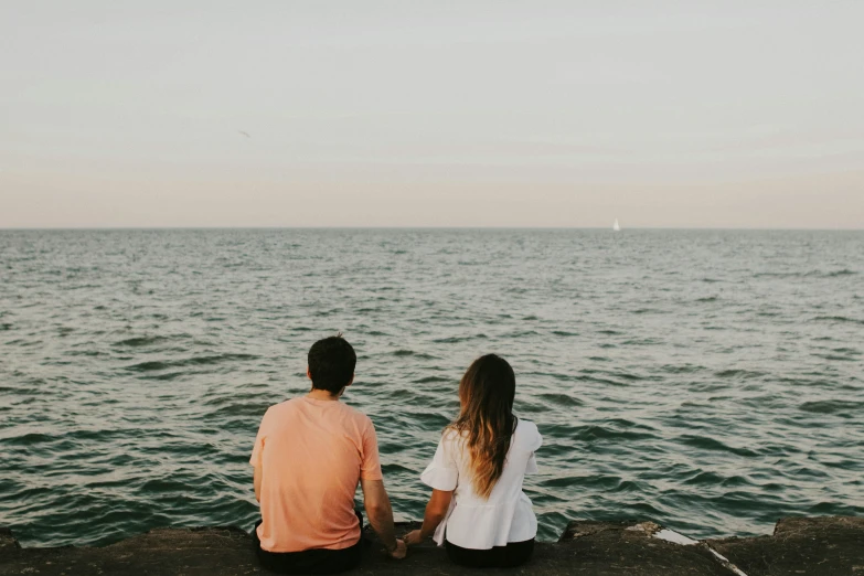 two people are sitting on rocks over looking the ocean