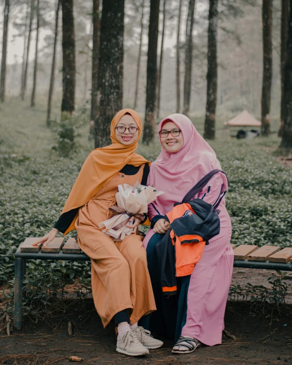 two women with orange and black outfits on sitting on a park bench