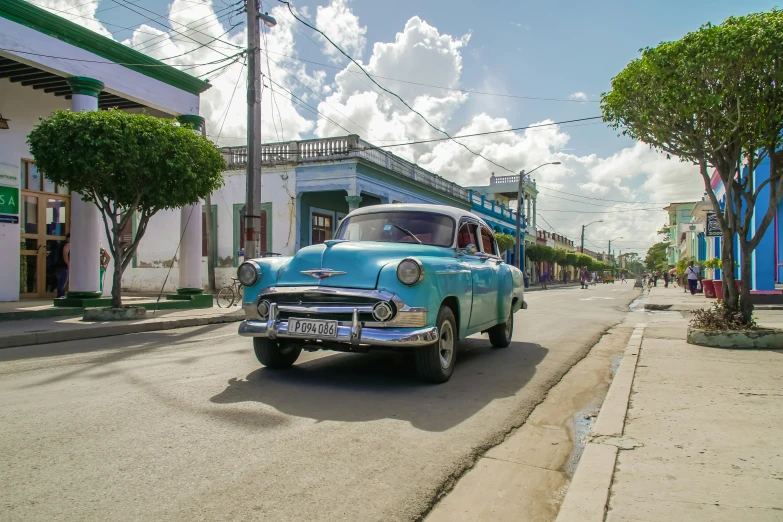 an old blue chevrolet sedan is traveling down the road