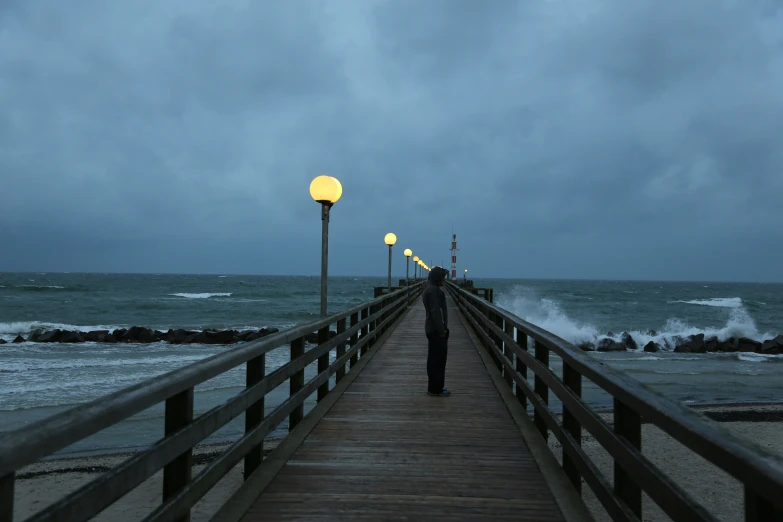 man standing on wooden pier overlooking water and stormy sky