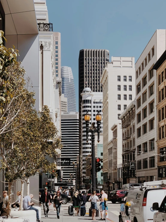 many people walk across the street by tall buildings