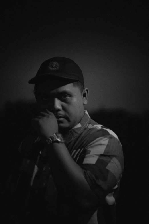 a young man wearing a cap standing in the dark
