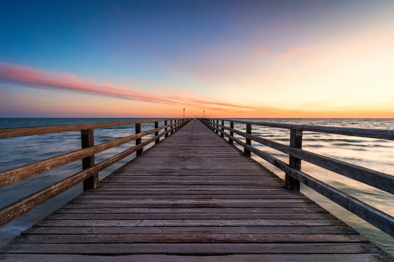 a pier in front of the ocean at sunset