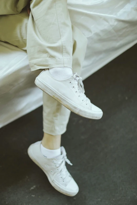 a person in white sneakers stands near a bed