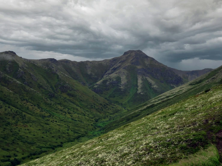 a rocky landscape covered in green mountains under a cloudy sky