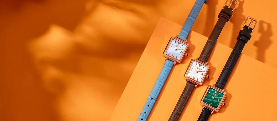 three watches one with green and the other brown sitting on an orange surface