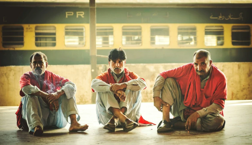 three men wearing colorful clothing sit together outside