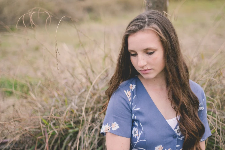 a woman sitting in the grass wearing a blue shirt