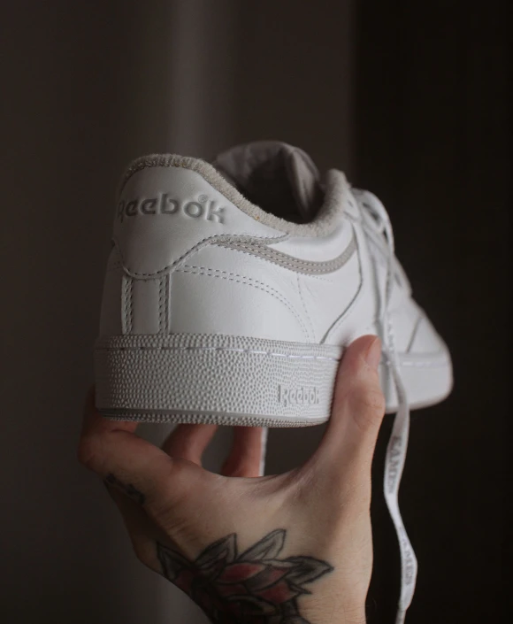 someone holds the bottom of a white adidas shoes