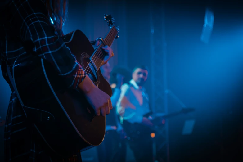 a guy is playing a guitar with another man behind him