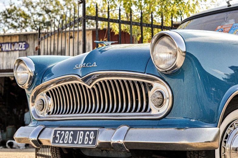 a blue classic car is parked next to a fence