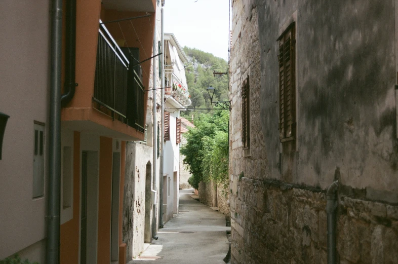 a narrow road running between buildings, with green vegetation growing in the distance