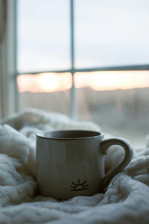 a white coffee cup on a white blanket with a window in the background