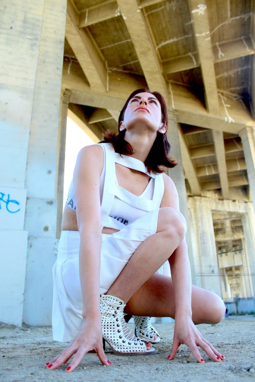 a woman in tight pants and a white top sitting under a bridge