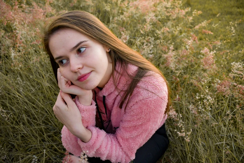 a girl in pink sweater sitting on grass in a field